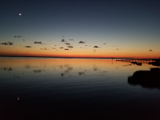 Beautiful dusk soundscape of the Outer Banks N.C. depicting a moon rising while sun is setting creating a brilliant band of color at the horizon with moon and clouds reflecting in the water. Zen vibes for all!